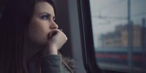 A dark-haired woman stares out the window of a train at the overcast city, perhaps worried about Low T in women.