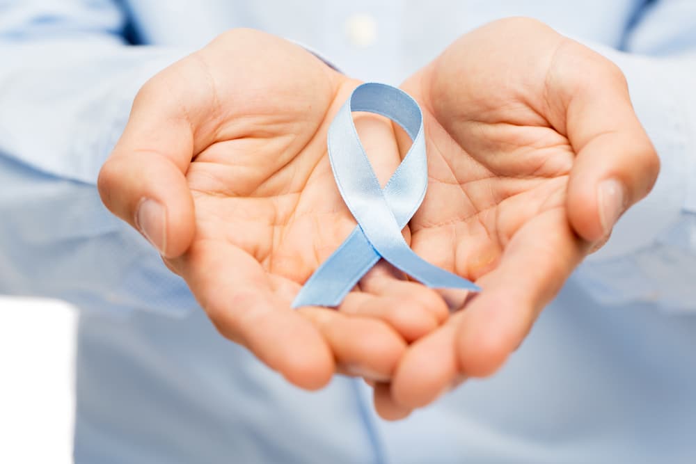 Una doctora sostiene en sus manos un lazo azul contra el cáncer de próstata. El cáncer de próstata no puede ser causado por la terapia de reemplazo de testosterona, pero TRT puede empeorar el cáncer de próstata existente.