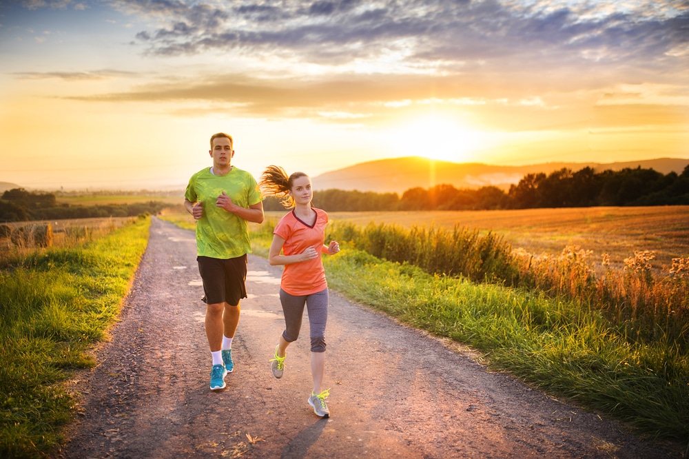 A man and woman wearing workout attire run down a gravel road in a Prosper 5K race with the sun rising in the background. 