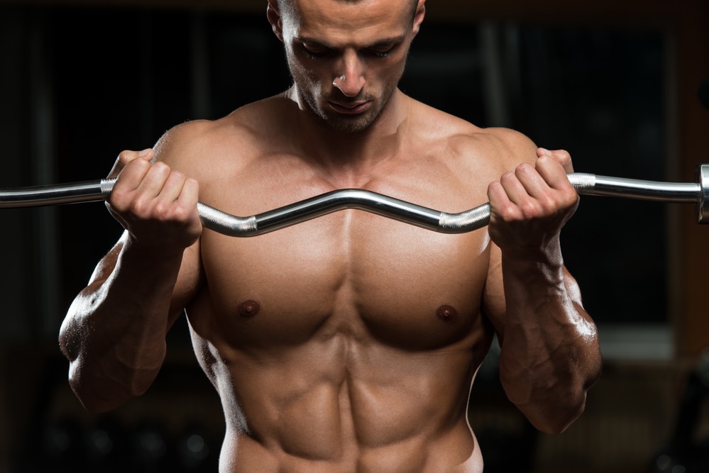 Un hombre musculoso y sin camiseta se ejercita en un gimnasio de Hurst, haciendo un ejercicio de pesas para sus bíceps.