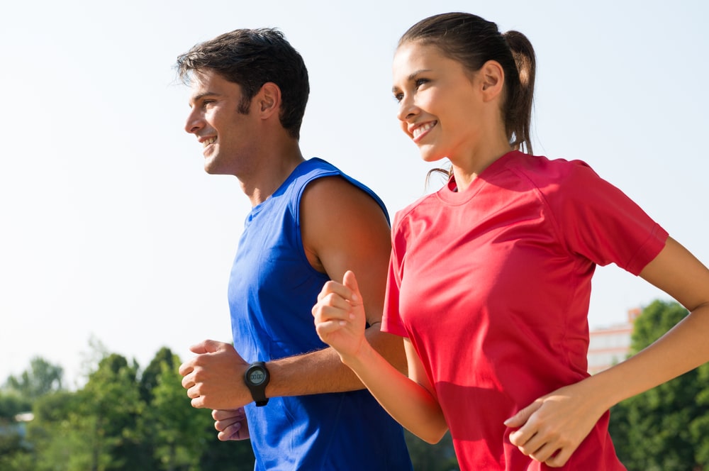 Una pareja joven, un hombre con camiseta azul y una mujer con camiseta roja están corriendo, posiblemente en un evento de 5k cerca de Prosper.