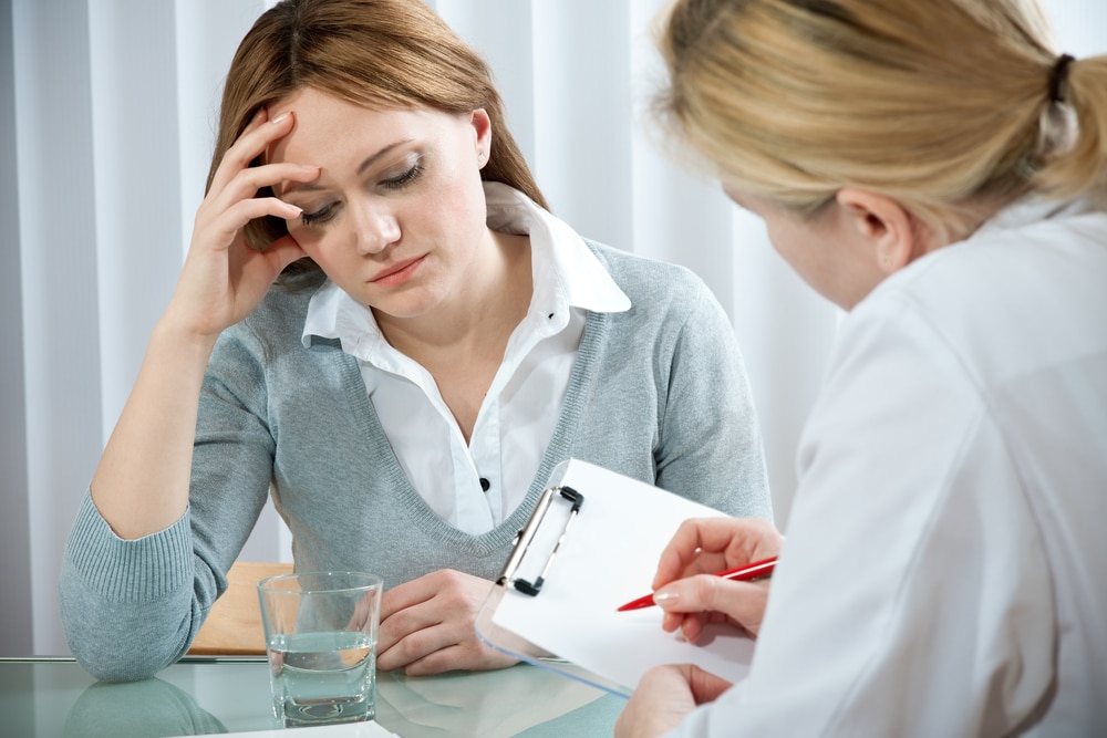 A young women wearing a sweater rests her head on her right hand. She is talking with a female doctor, possibly about testosterone replacement therapy for women.