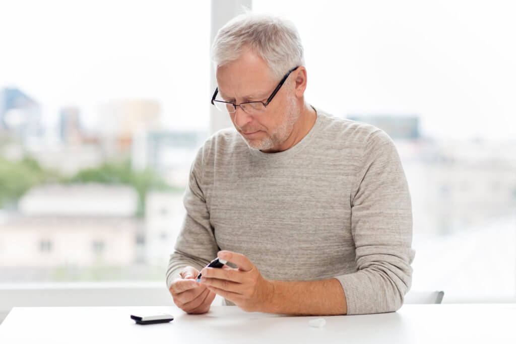 A middle-aged man with short gray hair and glasses tests his blood sugar by pricking his finger. Low testosterone may play a role in the development of type 2 diabetes.