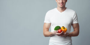 Young man in a white t-shirt holds fresh vegetables. Medical research shows that a low-fat diet can contribute to low testosterone under some circumstances.
