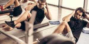 Three men are performing sit ups on the floor of a gym. Exercise is not a cure for clinical low testosterone.