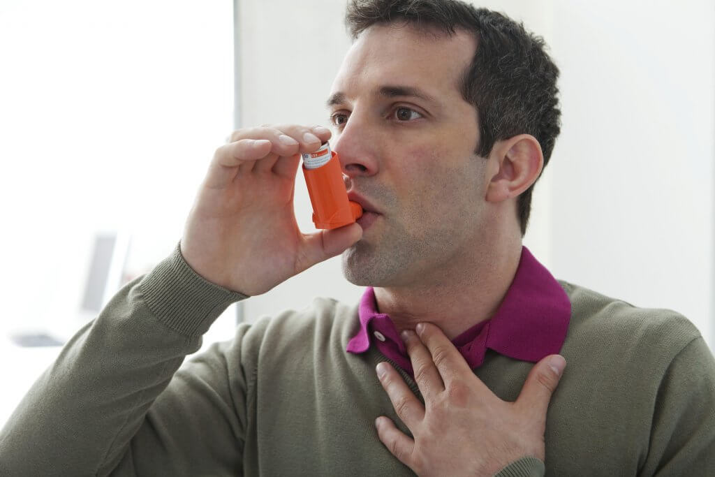 A man in a gray sweater uses an inhaler to get relief for a breathing problem. COPD has been linked to low testosterone.