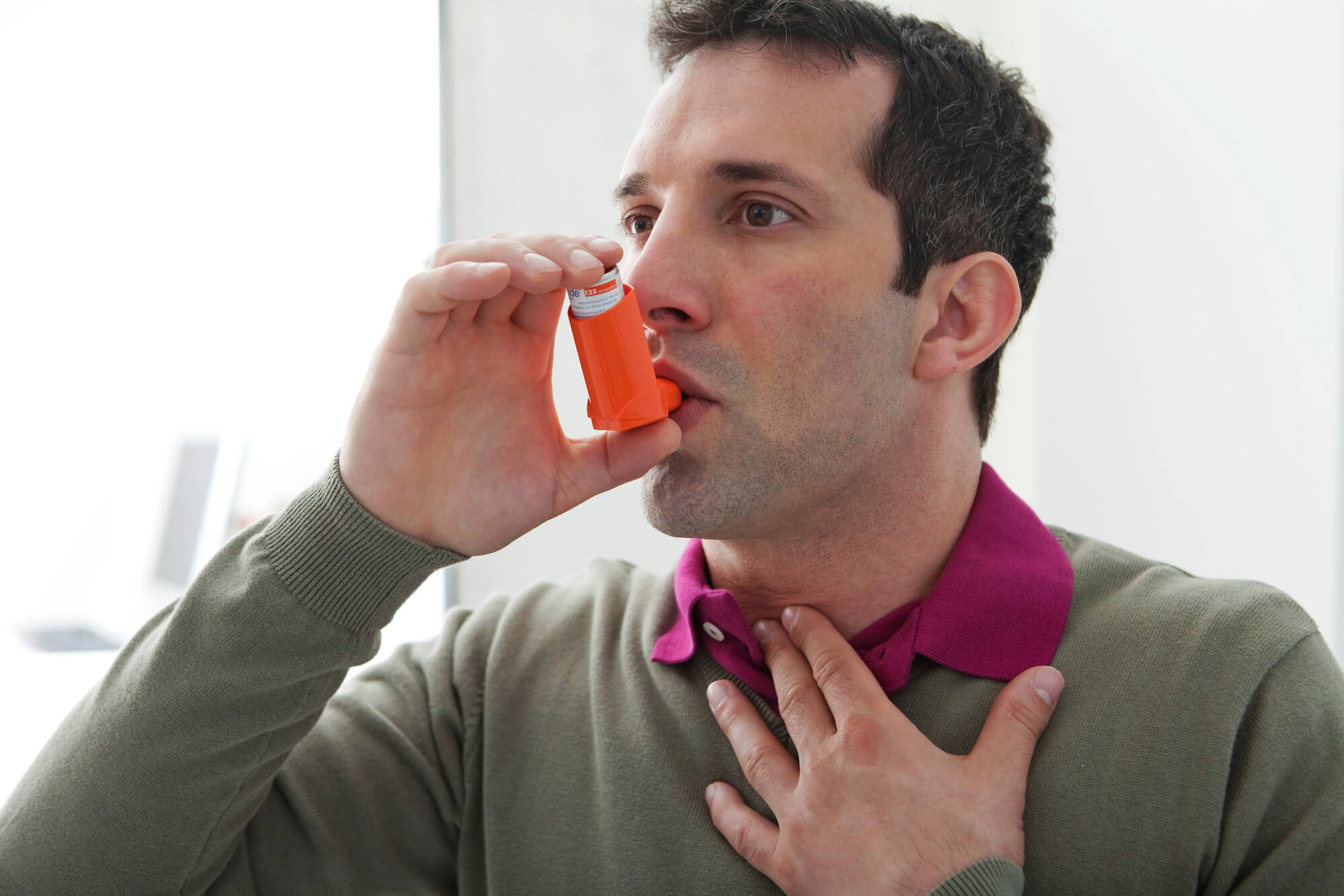 A man in a gray sweater uses an inhaler to get relief for a breathing problem. COPD has been linked to low testosterone.