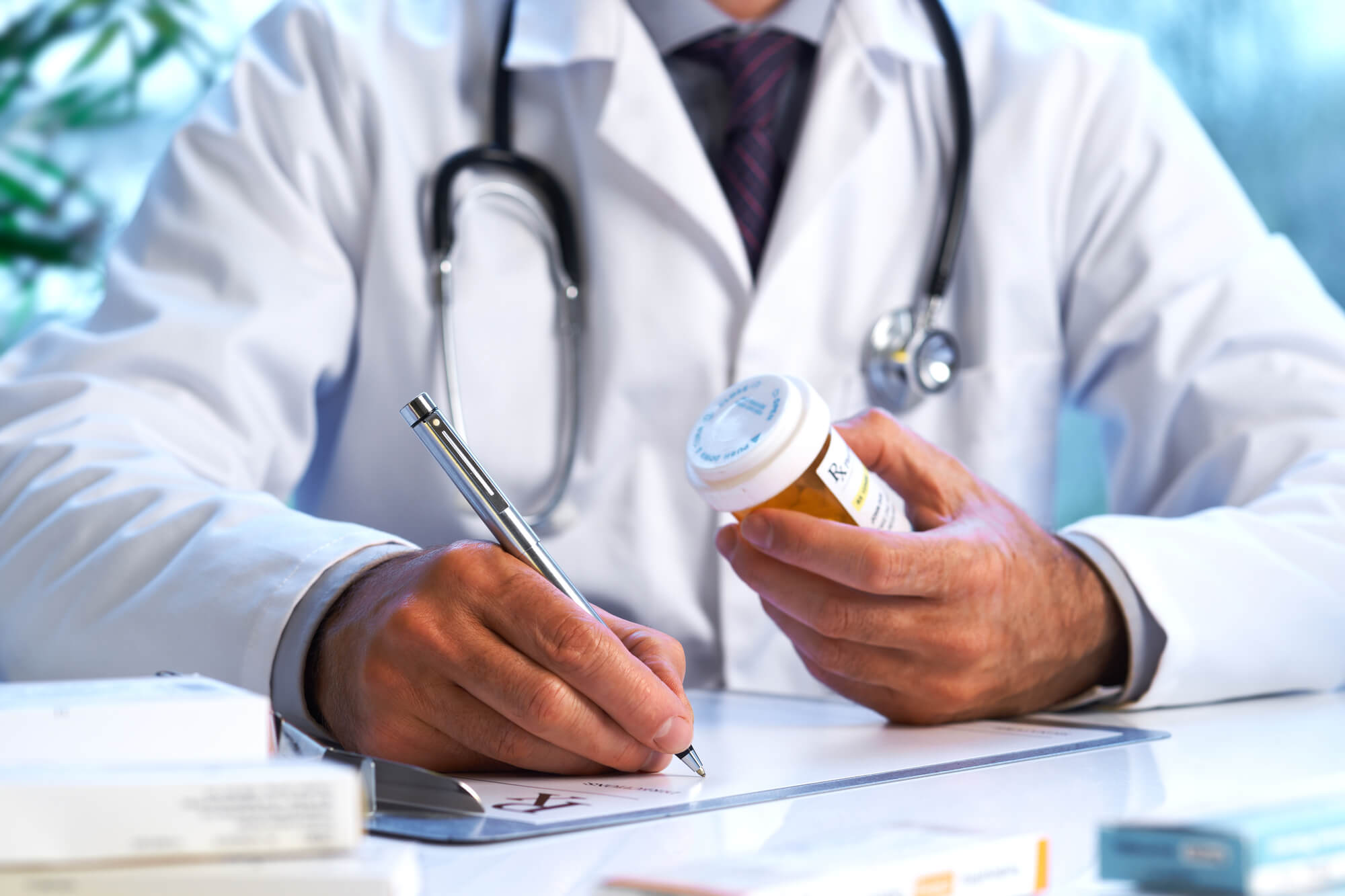 A doctor with a stethoscope around his neck writes a prescription, possibly unaware of the connection between opiates and low testosterone.