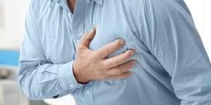 A man in a blue shirt clutches his chest. If he's had a history of heart trouble, he may be worried whether TRT is safe for him.