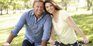 A man in a blue shirt and his female companion ride bikes in the park. Their quality of life has improved since learning the connection between hypothyroidism and low testosterone.