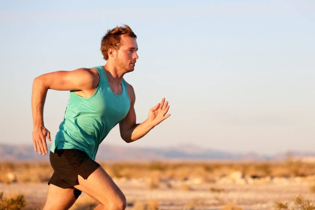 White male in a blu tank top is running across a desert landscape. Many people ask, "Does running boost testosterone?"