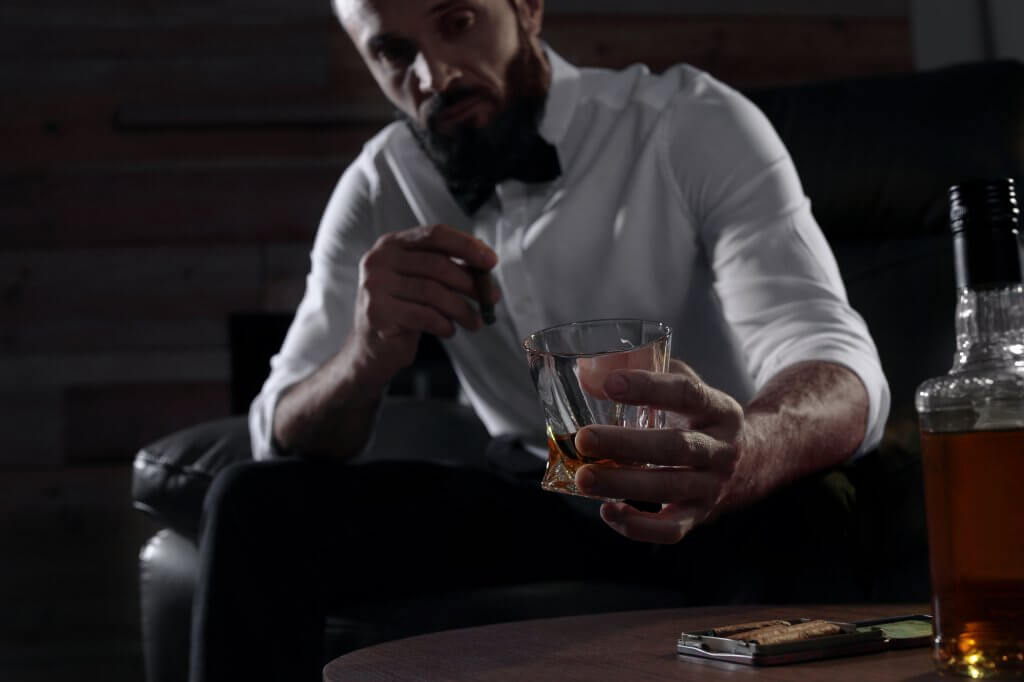 Man in a white shirt and bow tie looks at the glass in his hand, wondering if drinking alcohol is causing his Low T symptoms.