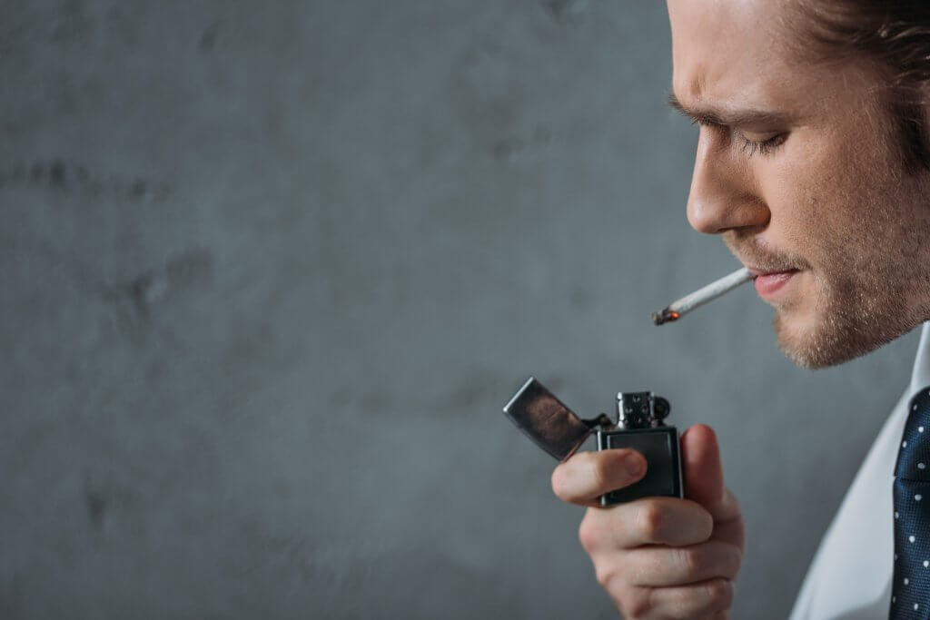 Un hombre con camisa y corbata enciende un cigarrillo. Pero, ¿fumar disminuye la testosterona? Sí, y no.