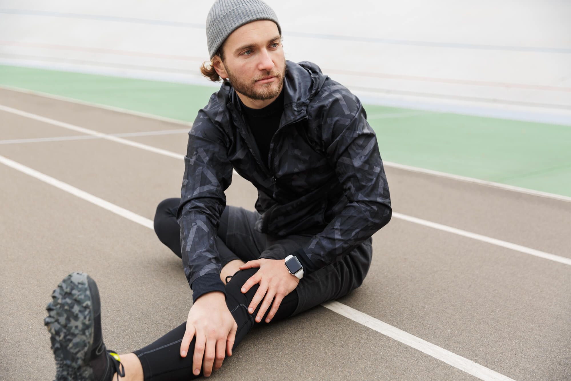 Un hombre vestido con un traje de entrenamiento negro estira mientras está sentado en una pista de atletismo con tiempo fresco. ¿Los niveles de testosterona fluctúan de forma natural o estacional?