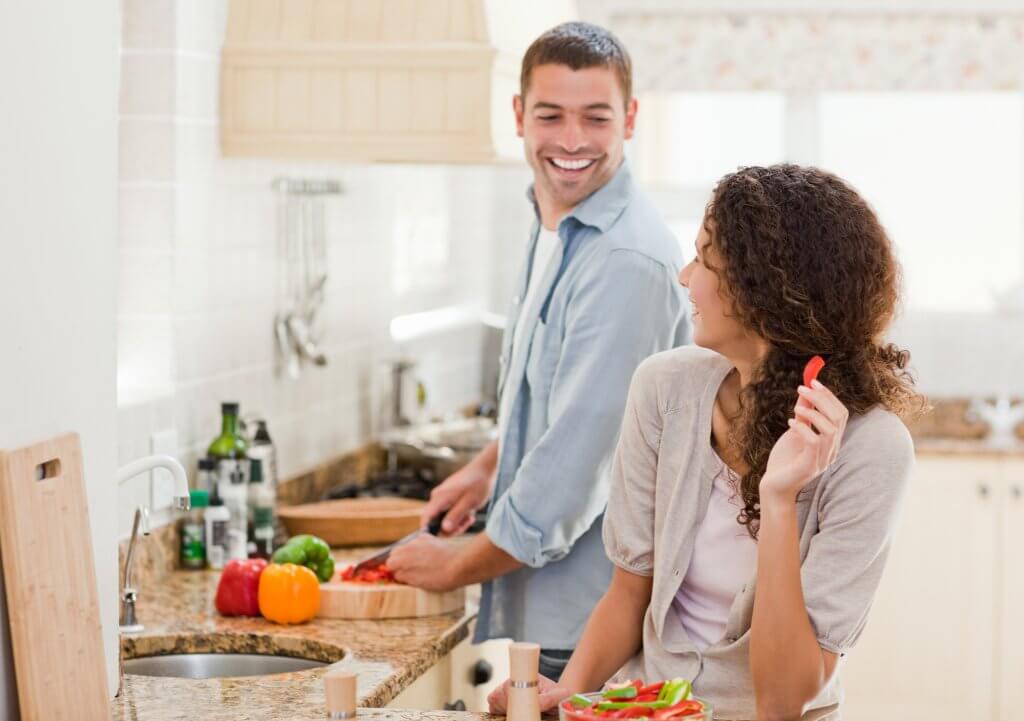 Un hombre sonriente y su feliz esposa preparan una comida sana en la cocina. Ha aprendido cómo sus hábitos alimenticios afectan a la testosterona
