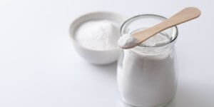 A jar of white powder, possibly sucralose or other artificial sweetener sits on a white surface with a wooden spoon on top.