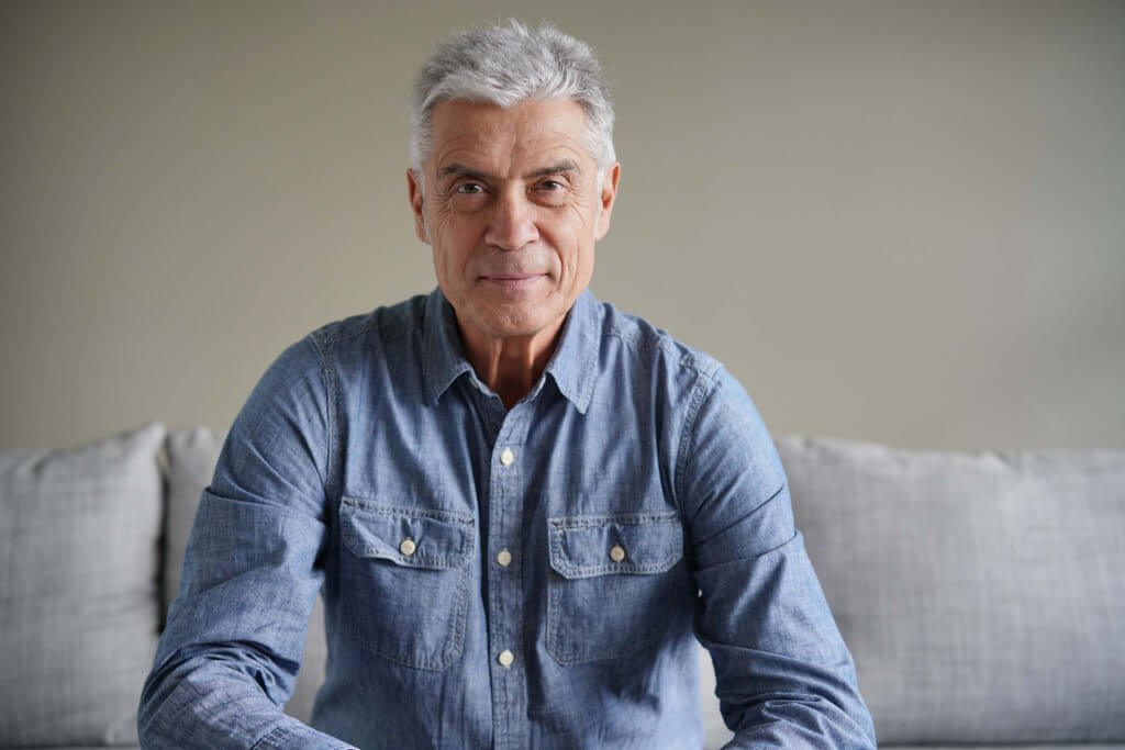 Portrait of casual modern senior man in denim on couch. You may be wondering what causes aging?