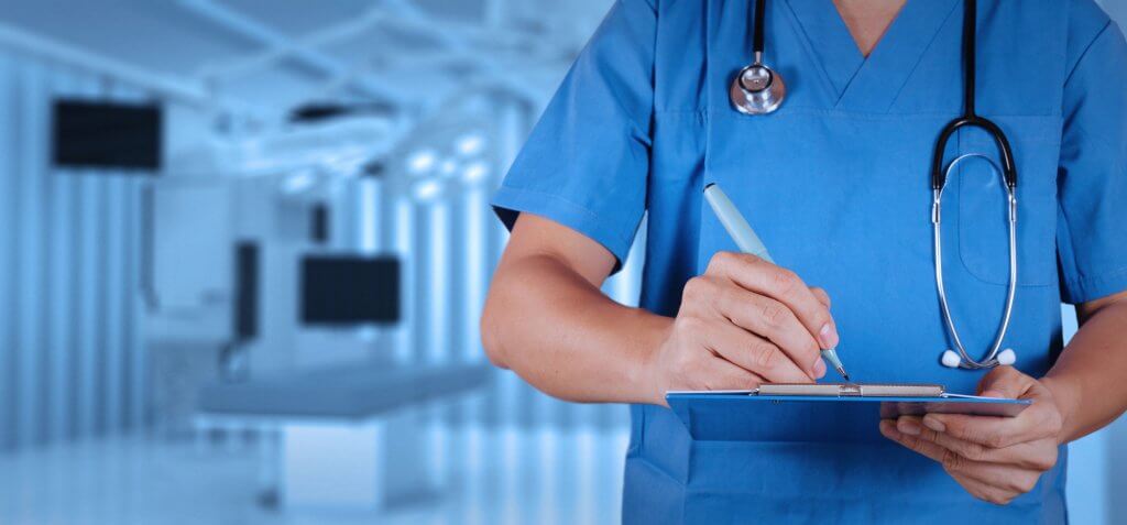 Doctor wearing blue scrubs is making notes on a clipboard regarding his patient's diabetes treatment.